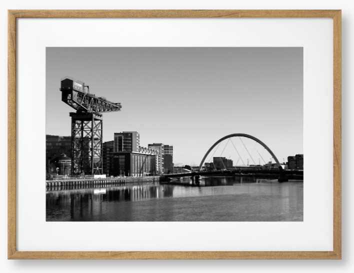 Black and White Framed Photo Of A Cityscape with a crane, buildings, and a bridge over water.