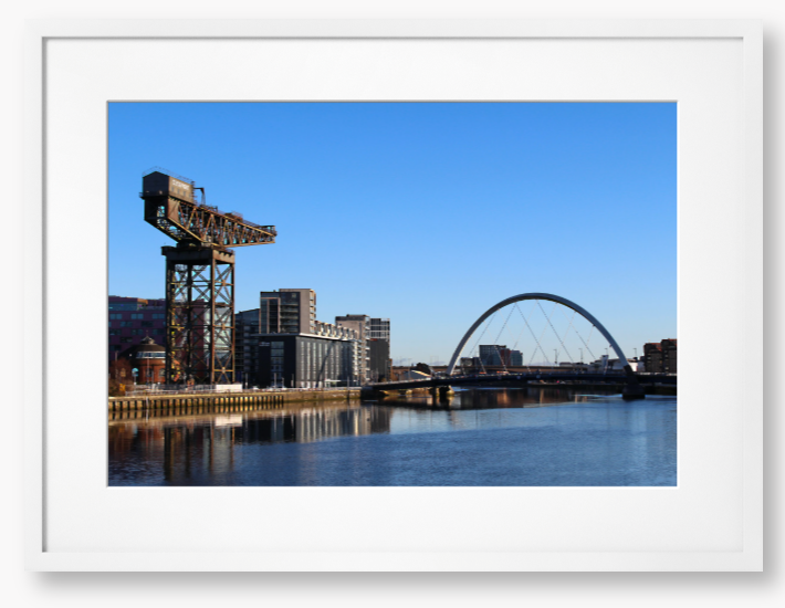 Framed Photo Of A Cityscape with a crane, buildings, and a bridge over water.
