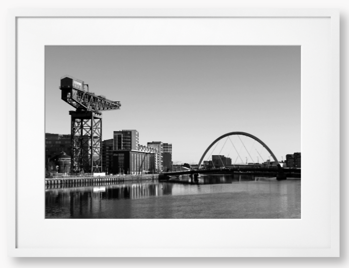 Black and White Framed Photo Of A Cityscape with a crane, buildings, and a bridge over water.