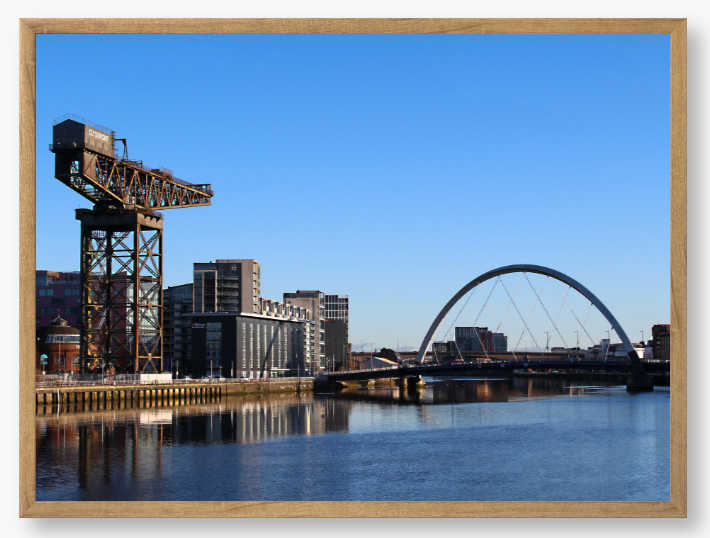 Framed Photo Of A Cityscape with a crane, buildings, and a bridge over water.