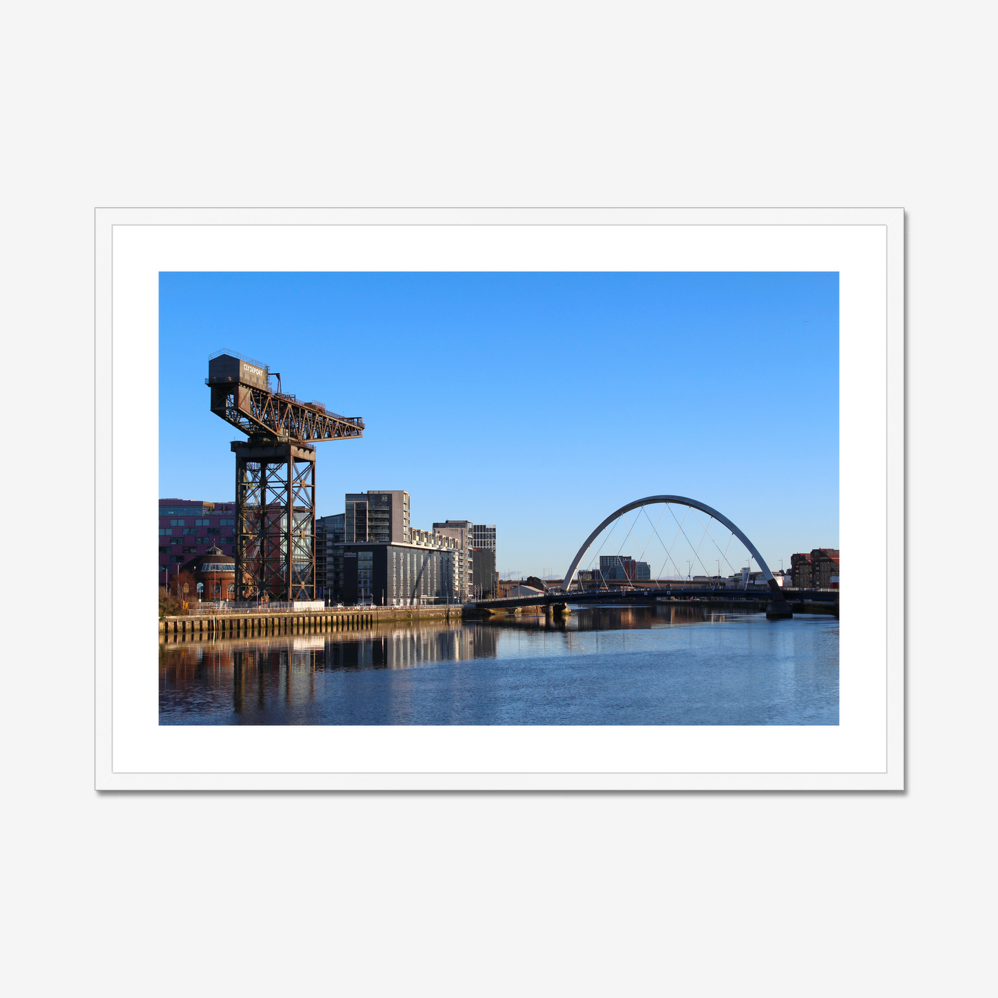 Framed photograph of a cityscape with a crane and a bridge over water.