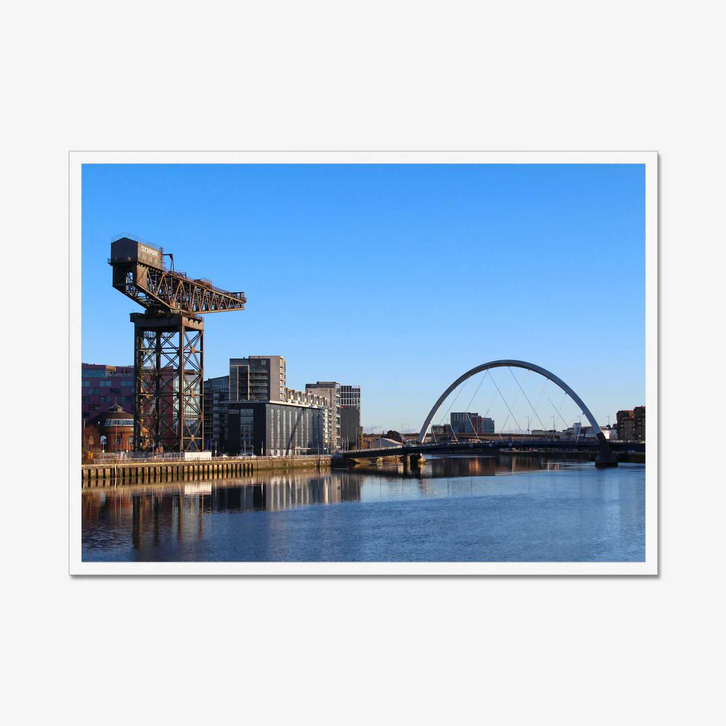 Framed photograph of a cityscape with a crane and a bridge over water.