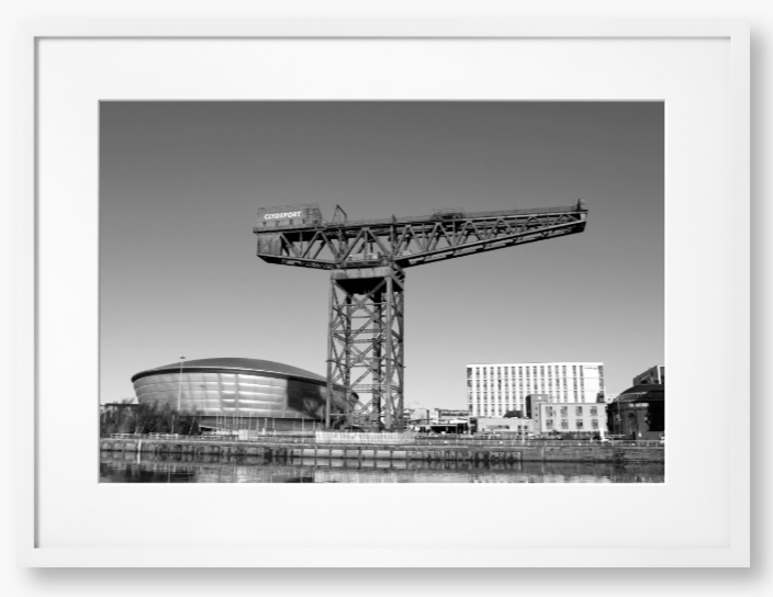 Black and white framed photo of a large crane with modern buildings in the background.