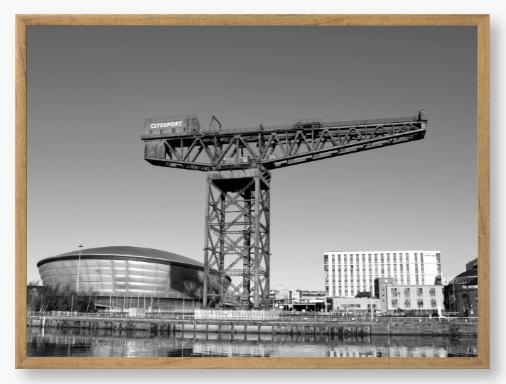 Black and white framed photo of a large crane with modern buildings in the background.