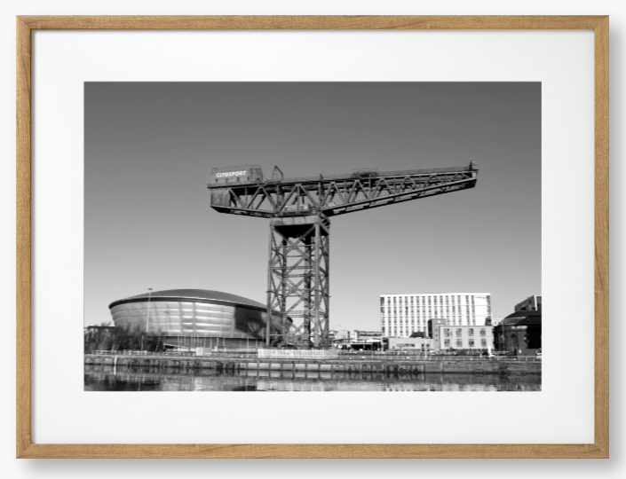 Black and white framed photo of a large crane with modern buildings in the background.