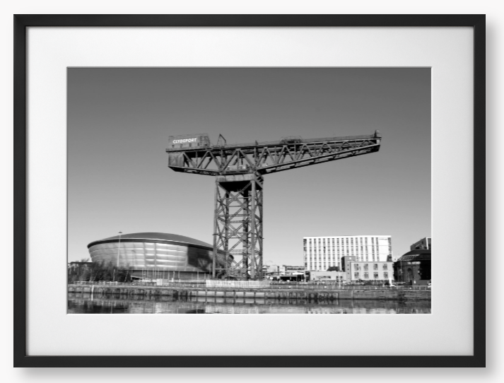 Black and white framed photo of a large crane with modern buildings in the background.