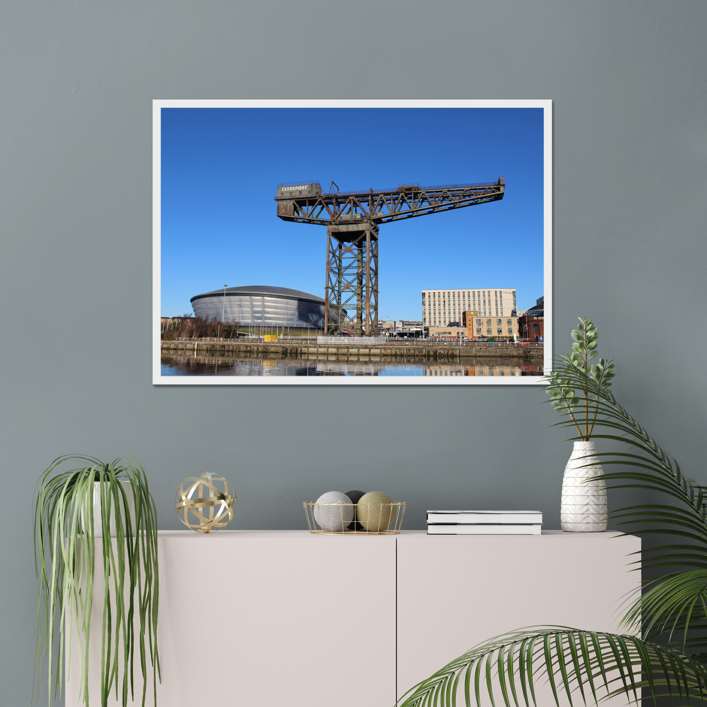 Framed photograph of a crane and building on a wall above a white cabinet with decorative items.