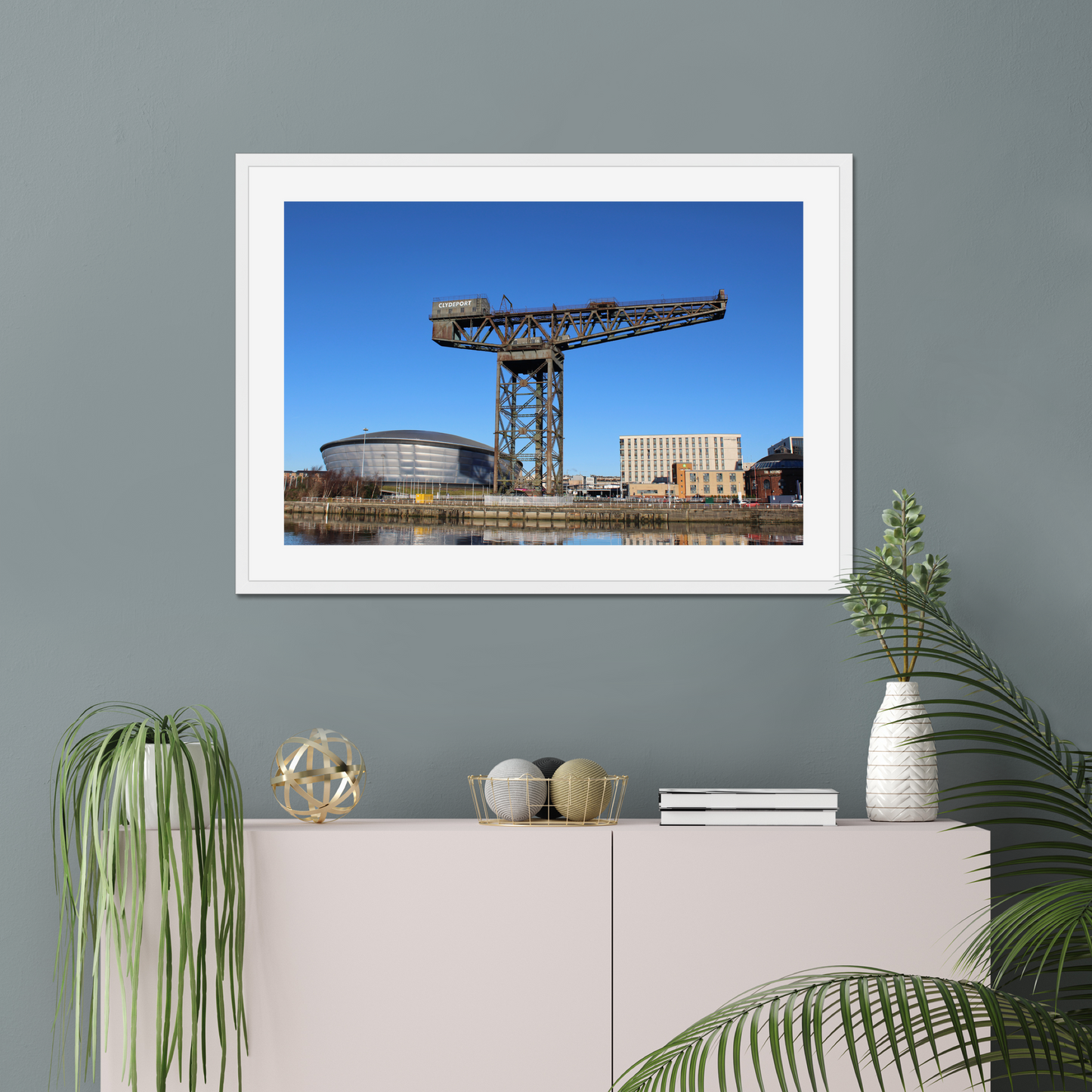 Framed photograph of a crane and building on a wall above a white cabinet with decorative items.