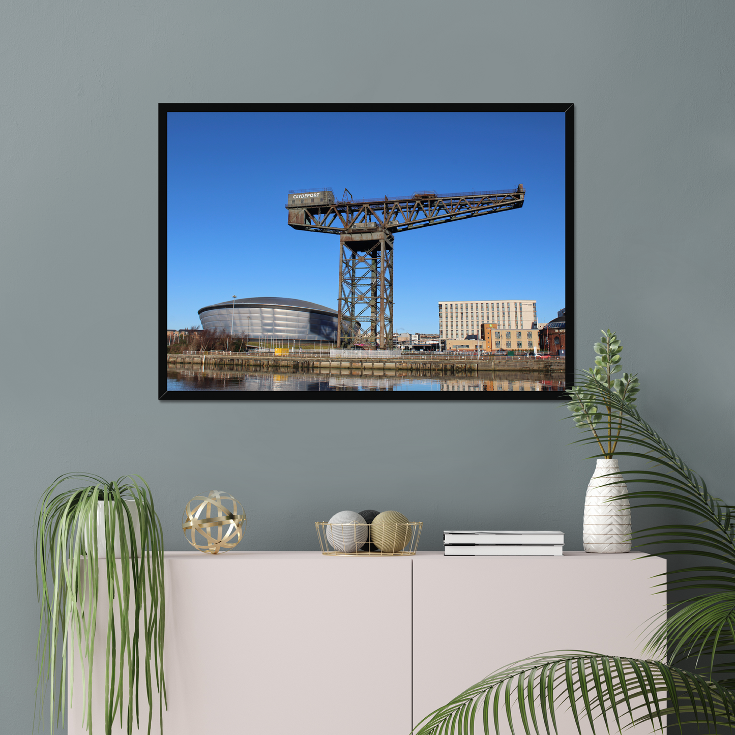 Framed photograph of a crane and building on a wall above a white cabinet with decorative items.