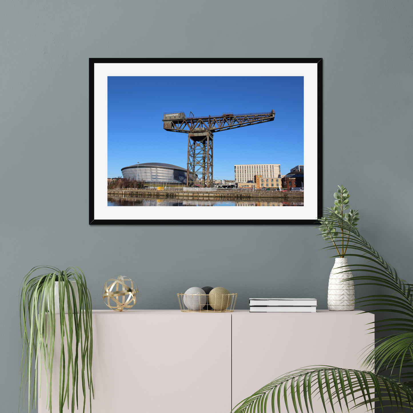 Framed photograph of a crane and building on a wall above a white cabinet with decorative items.