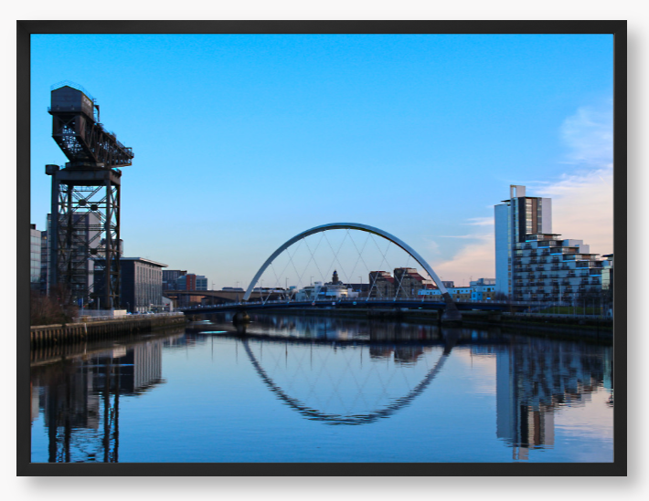 A framed print featuring a photograph of Glasgow's River Clyde with reflections, including a prominent crane and modern cityscape in the background.