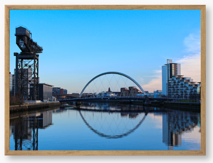 A framed print featuring a photograph of Glasgow's River Clyde with reflections, including a prominent crane and modern cityscape in the background.
