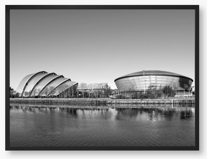 Black and white framed photograph of modern architectural buildings by a body of water.