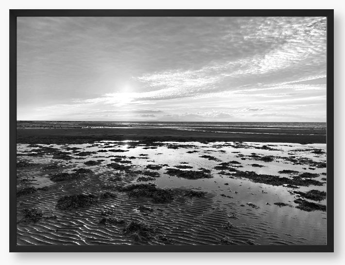 Black and white framed photograph of a coastal landscape with a sunset.