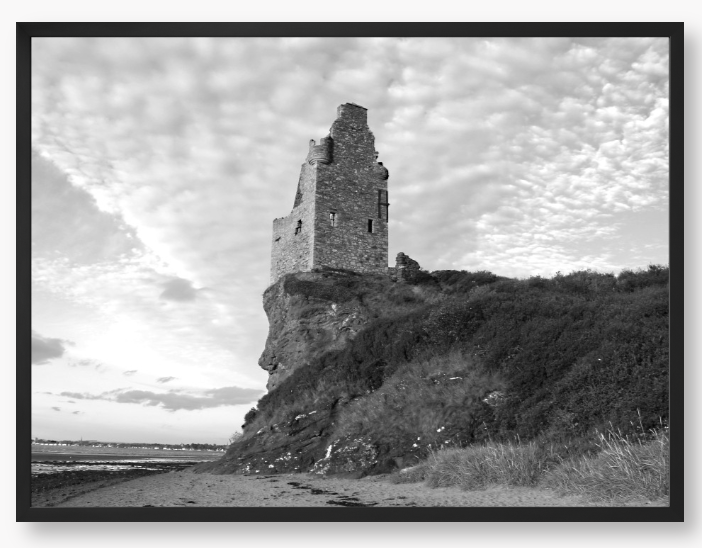 Framed black and white photograph of a tower on a cliff with a cloudy sky.