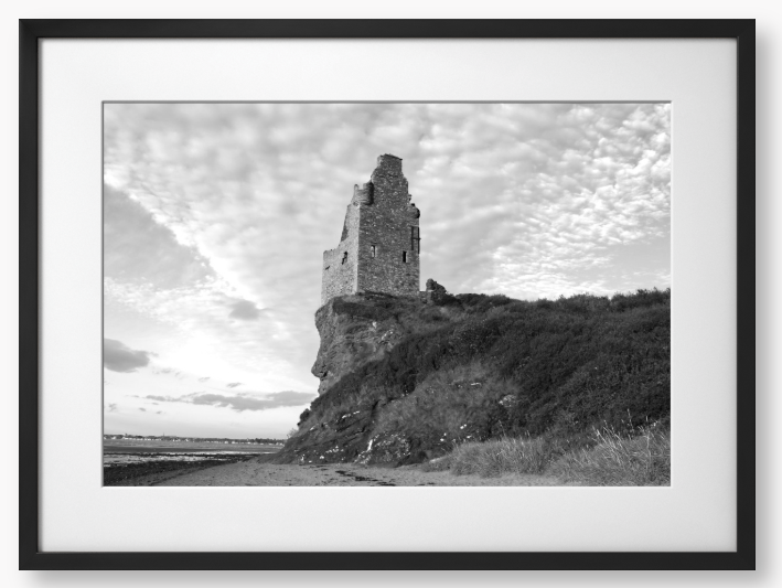 Framed black and white photograph of a tower on a cliff with a cloudy sky.