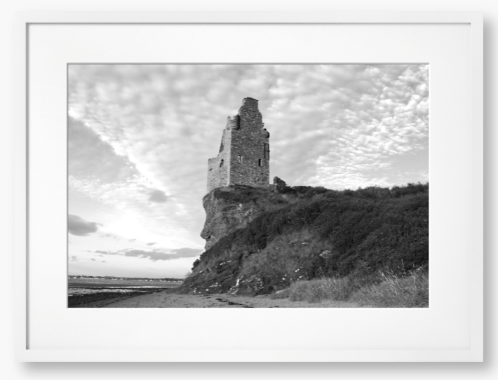 Framed black and white photograph of a tower on a cliff with a cloudy sky.