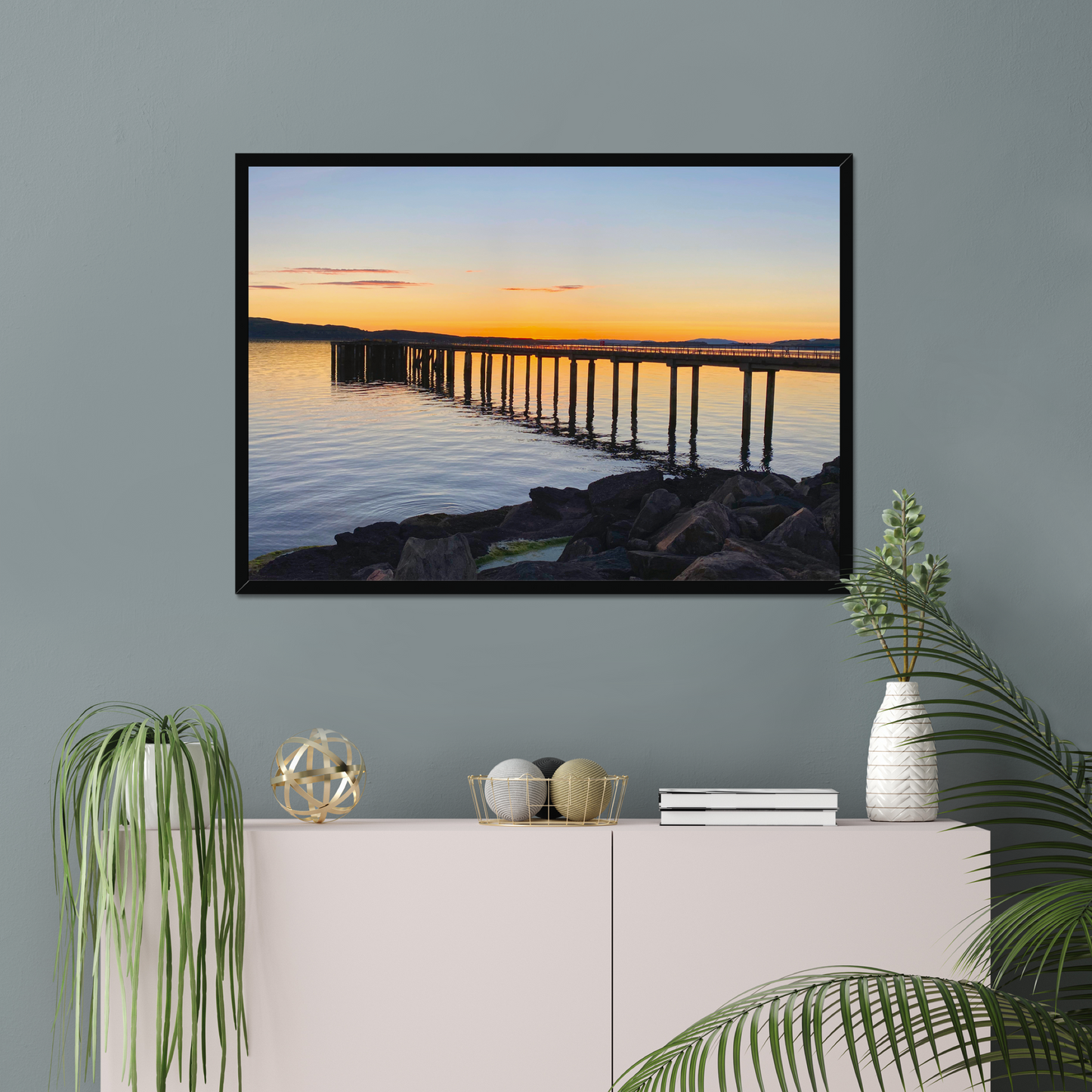 Framed artwork of a sunset over a pier on a wall above a white console table with decorative items.