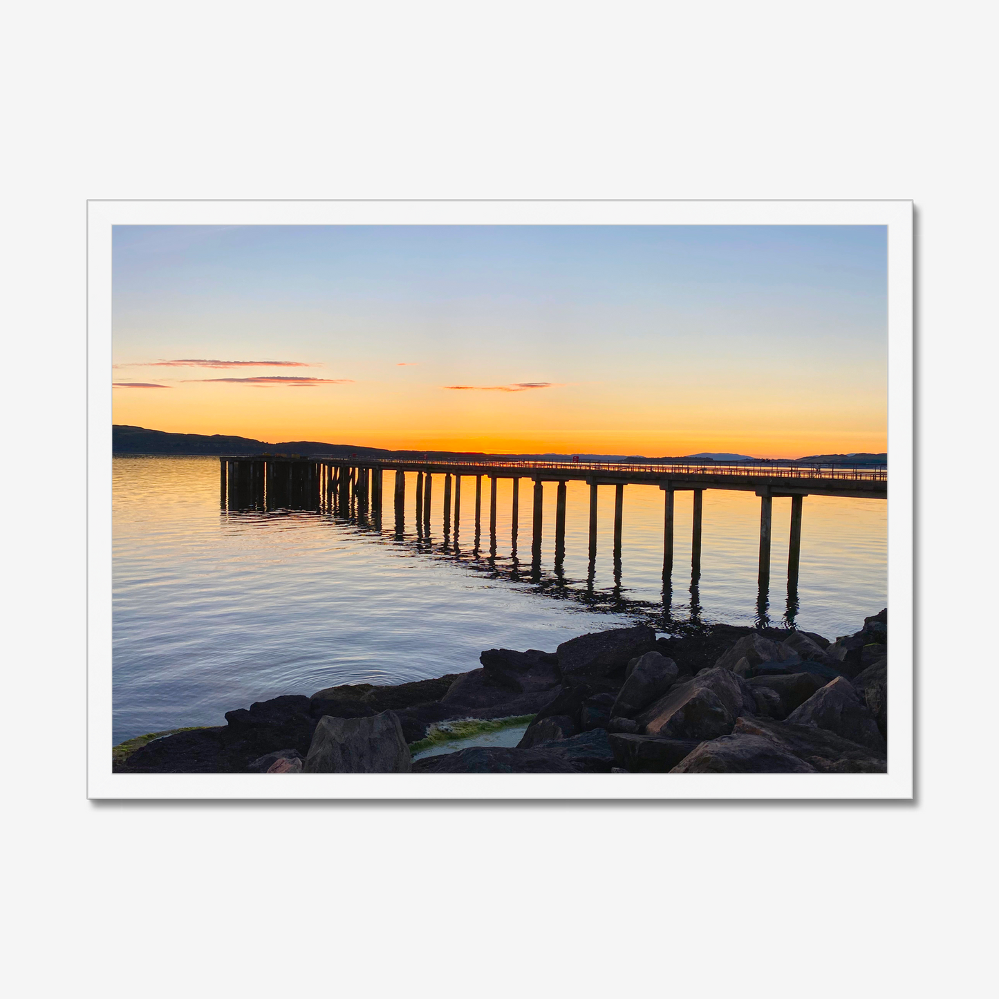 Sunset over a dock with calm water and rocks in the foreground