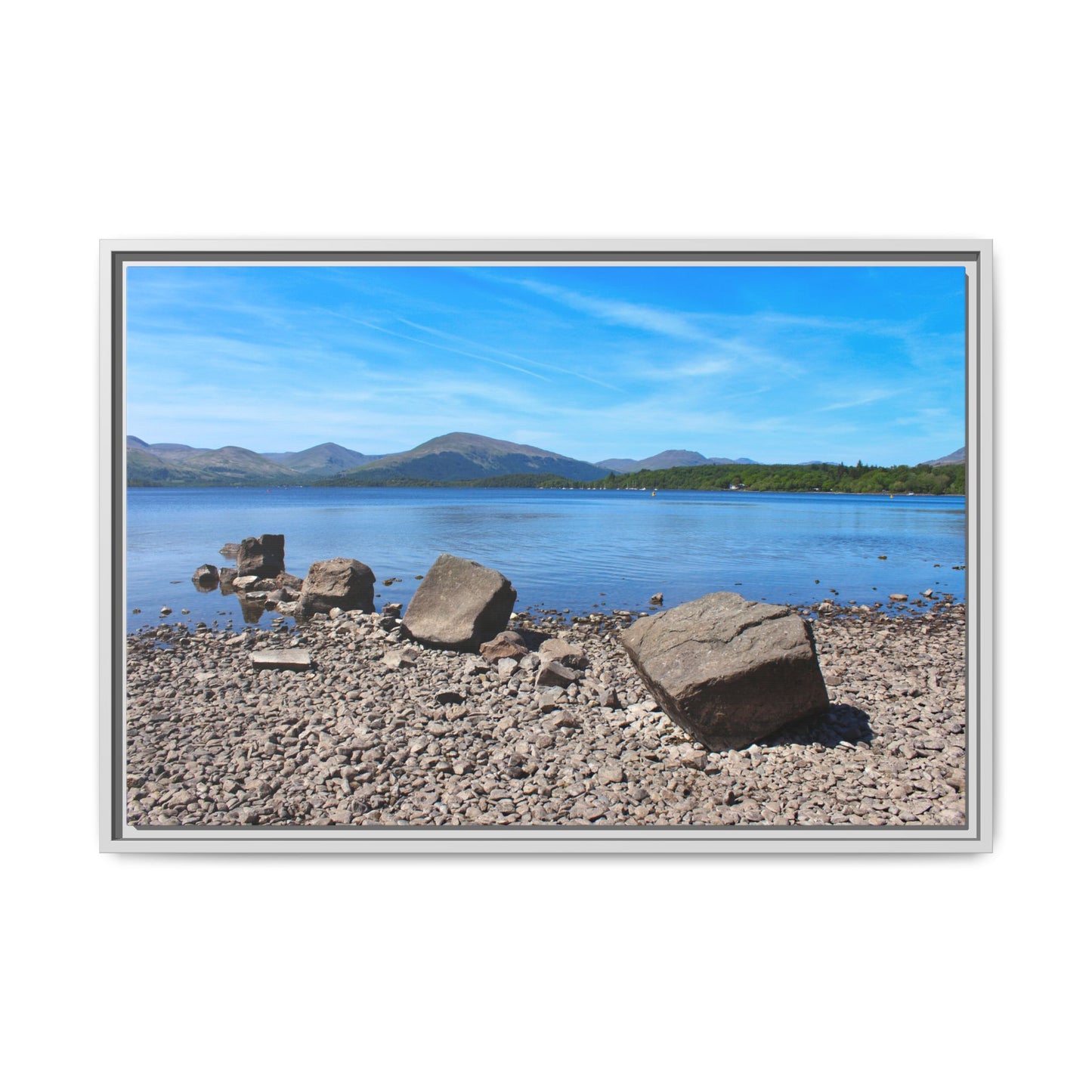 Framed photograph of a lake with mountains and rocks on a pebbly shore.