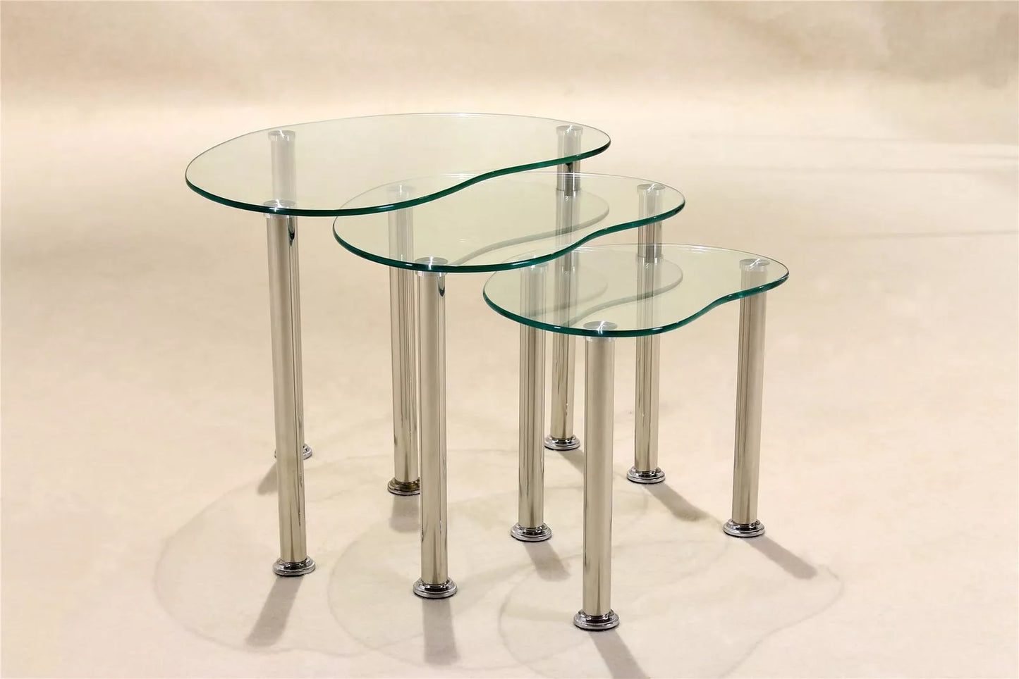 A set of three clear glass tables with stainless steel legs, varying in size.