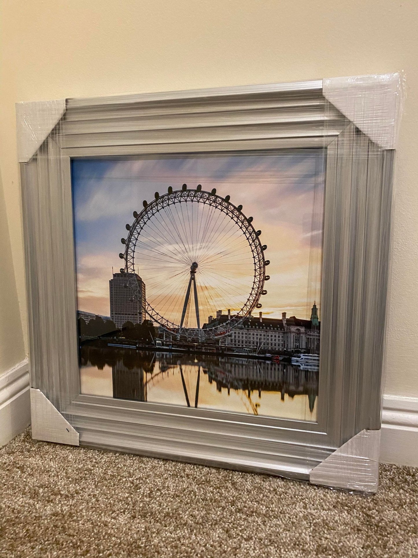 Framed picture of a Ferris wheel with a sunset sky, leaning against a beige wall.