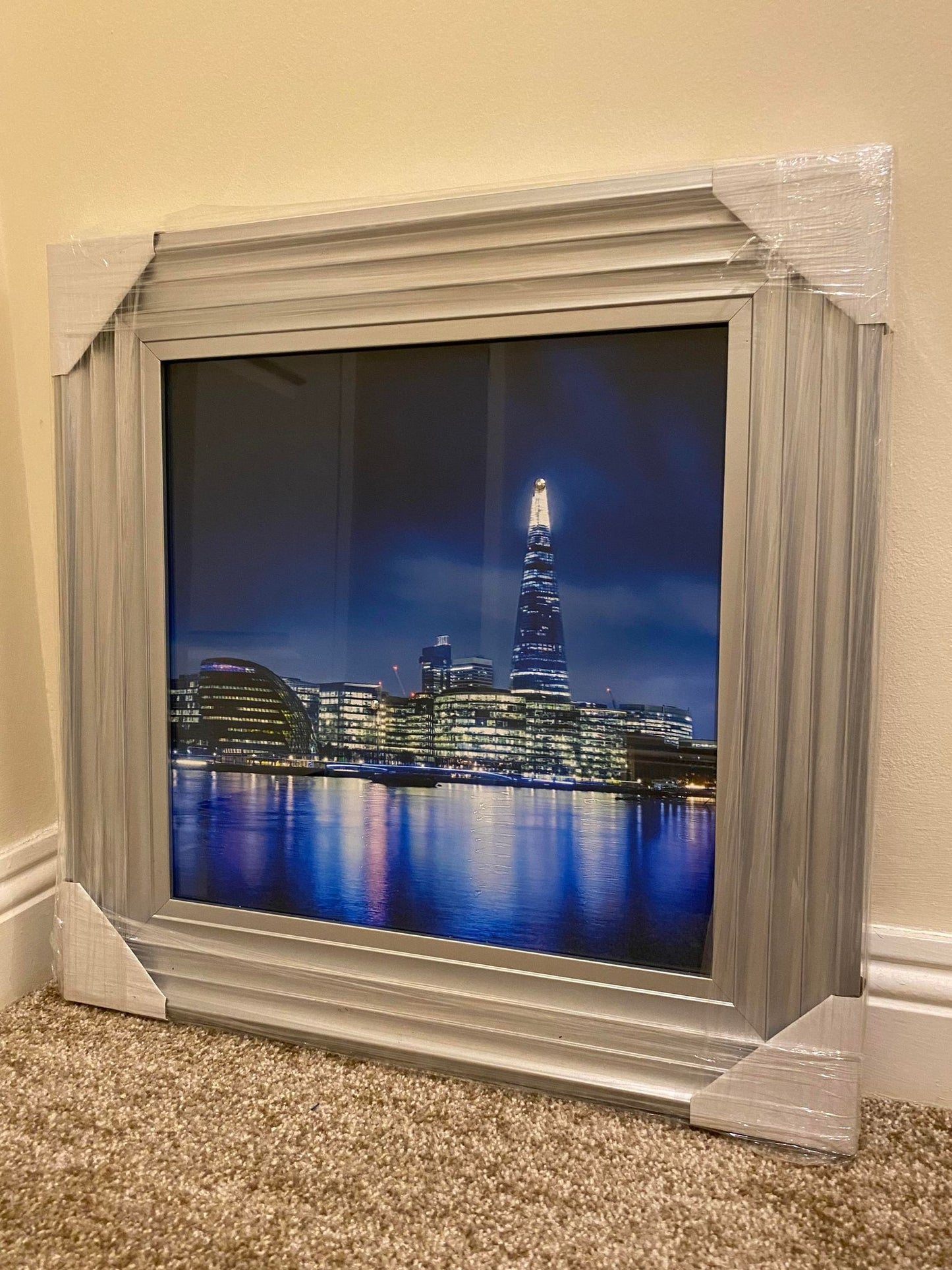 Silver framed picture of a cityscape at night with a tall building reflected in water.