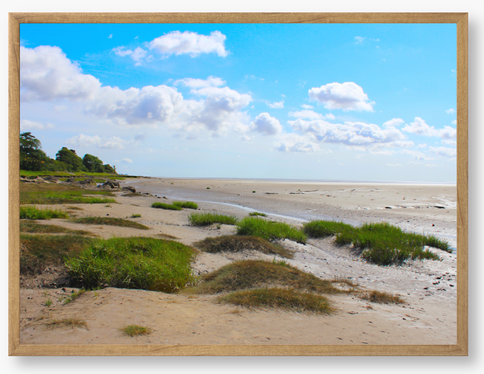 Framed photograph of a coastal landscape with sandy beach, grassy areas, and blue sky.