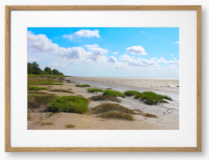 Framed photograph of a coastal landscape with sandy beach, grassy areas, and blue sky.