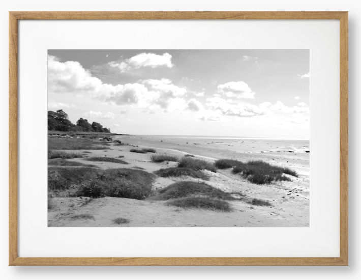Black and White Framed photograph of a coastal landscape with sandy beach, grassy areas, and cloudy sky.