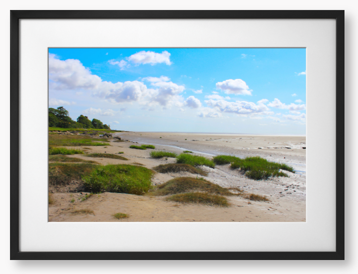 Framed photograph of a coastal landscape with sandy beach, grassy areas, and blue sky.