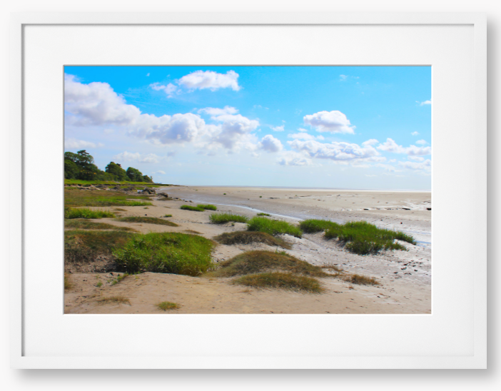 Framed photograph of a coastal landscape with sandy beach, grassy areas, and blue sky.