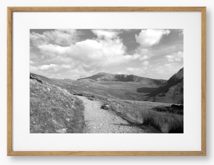 Black and White Framed photo of a mountain landscape with a path leading towards distant mountains with a cloudy sky