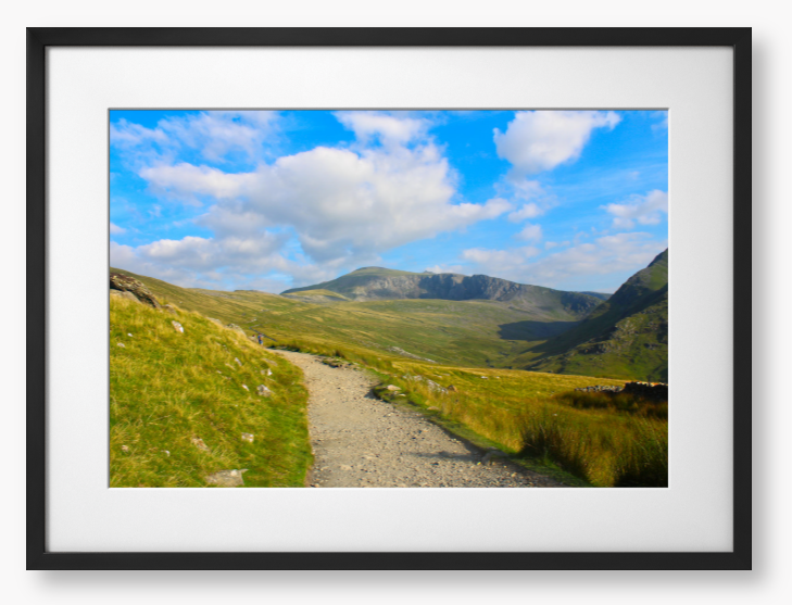 Framed photo of a mountain landscape with a path leading towards distant mountains under a blue sky with clouds