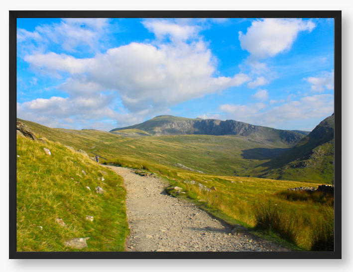 Framed photo of a mountain landscape with a path leading towards distant mountains under a blue sky with clouds