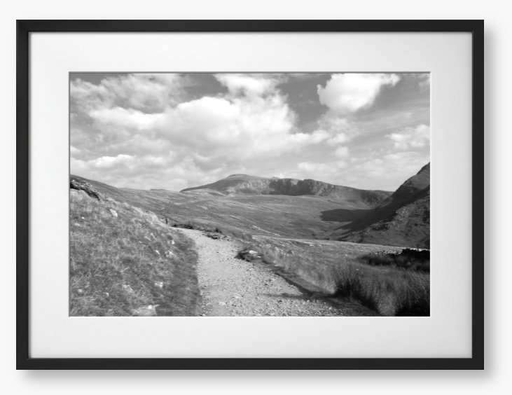 Black and White Framed photo of a mountain landscape with a path leading towards distant mountains with a cloudy sky