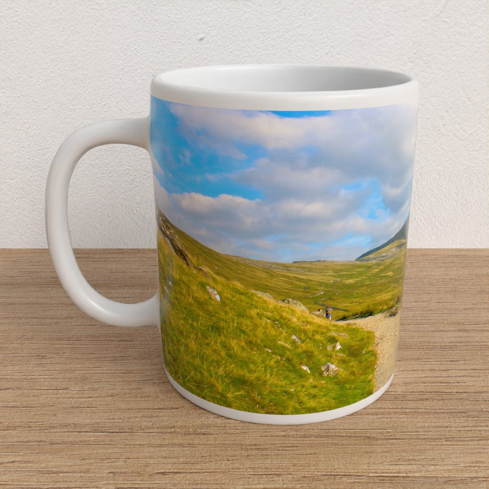 White mug with a scenic design of a green landscape and blue sky on a wooden surface.