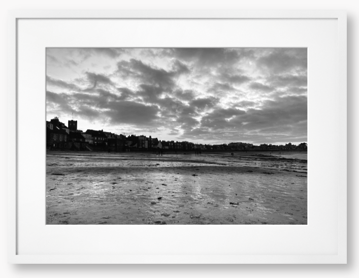 Black and white framed photograph of a coastal scene with buildings and clouds.