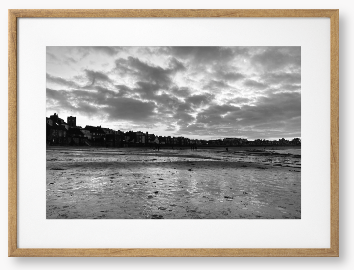 Black and white framed photograph of a coastal scene with buildings and clouds.