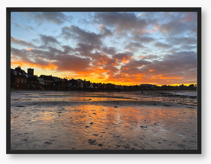 Framed Photo of a sunset over a coastal town with vibrant colours reflected in the water.