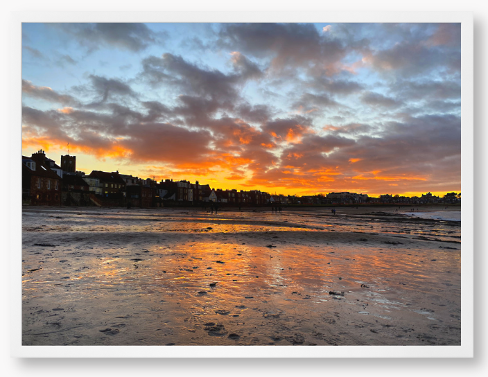 Framed Photo of a sunset over a coastal town with vibrant colours reflected in the water.