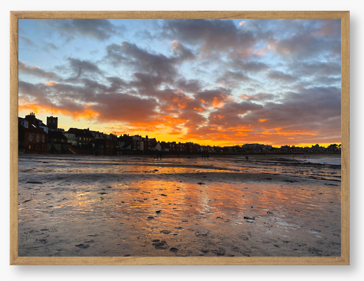 Framed Photo of a sunset over a coastal town with vibrant colours reflected in the water.