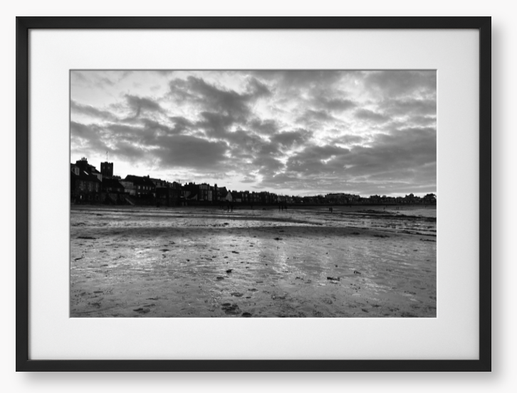 Black and white framed photograph of a coastal scene with buildings and clouds.