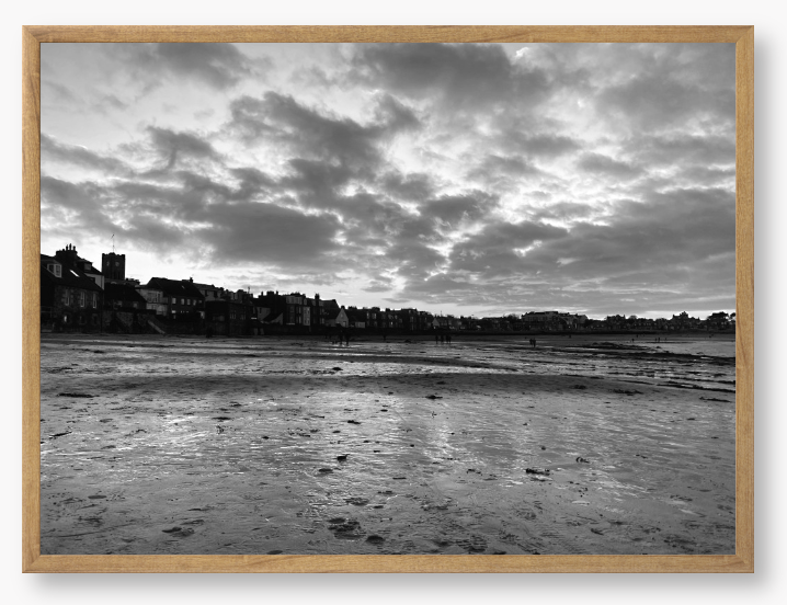 Black and white framed photograph of a coastal scene with buildings and clouds.