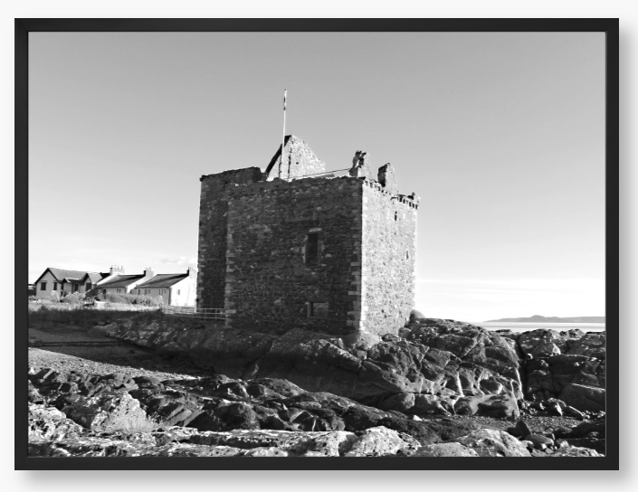 black and white Framed Photo of a Stone castle on rocky terrain with a clear blue sky