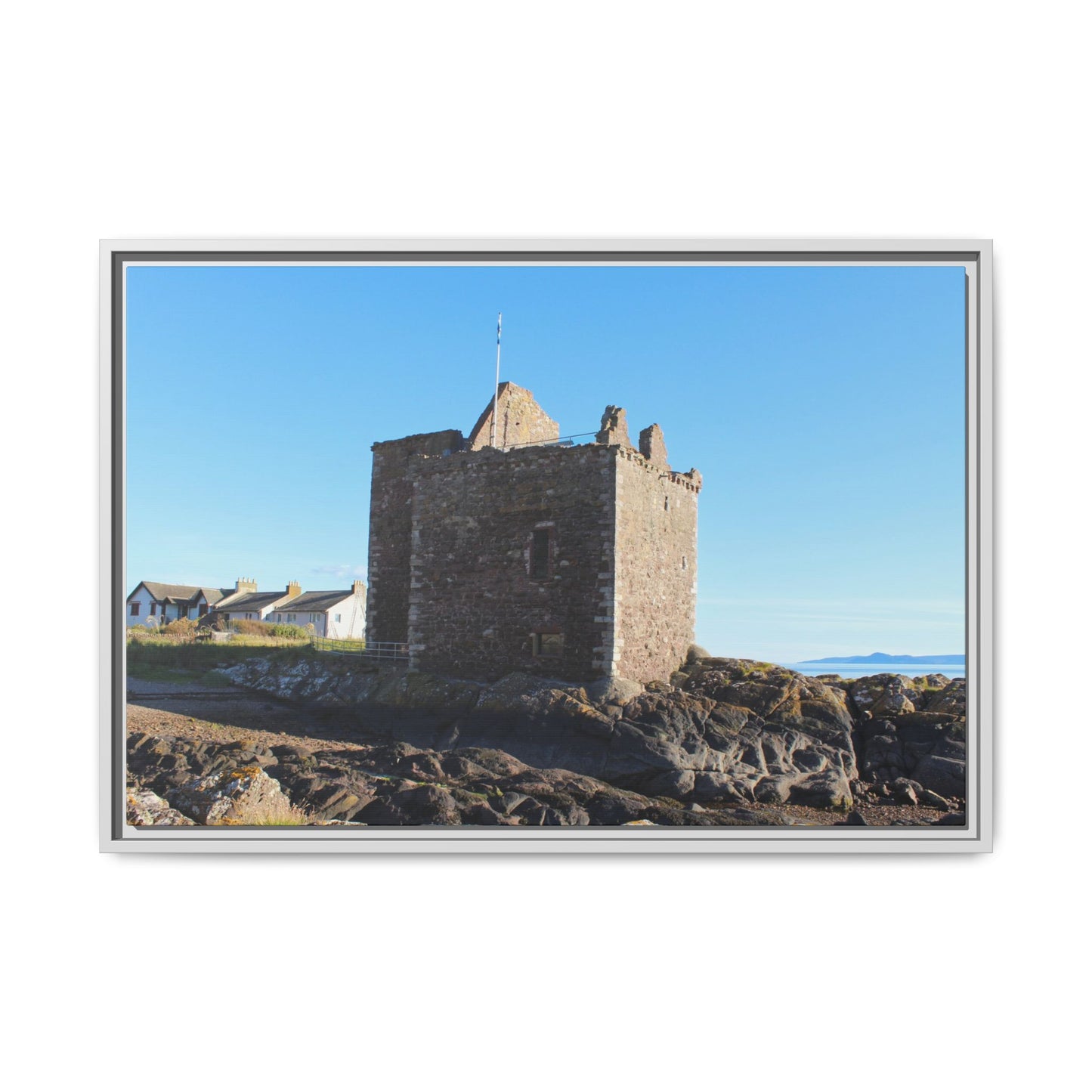 Framed photograph of a stone tower on rocky terrain with a clear blue sky.