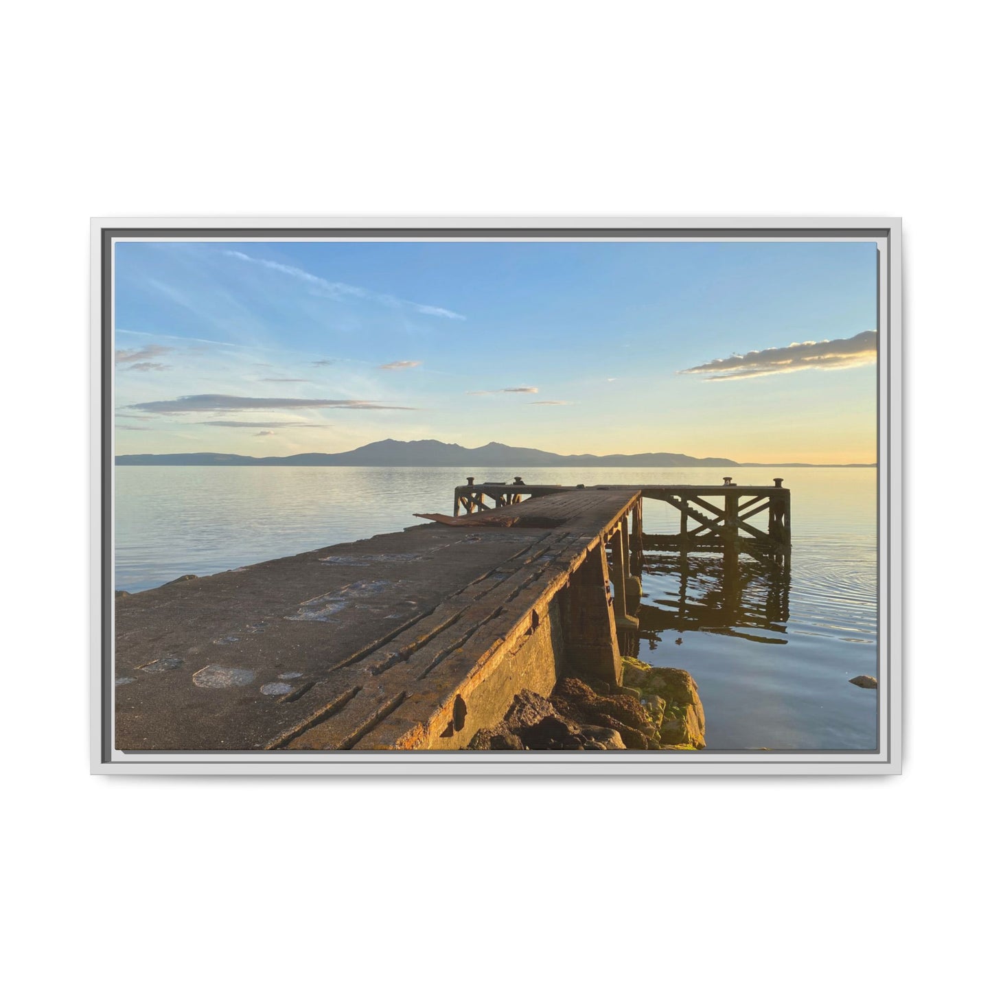 Wooden dock extending into a calm body of water with mountains in the distance, framed in silver.