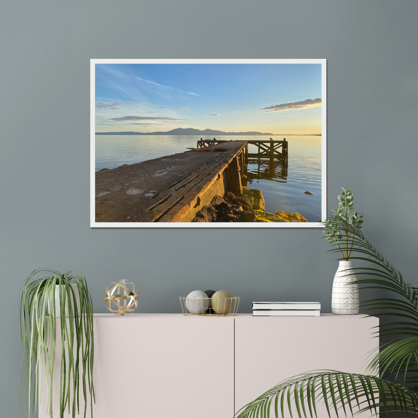 Framed artwork of a cityscape with a bridge against a sunset sky, displayed on a wall above a white cabinet.