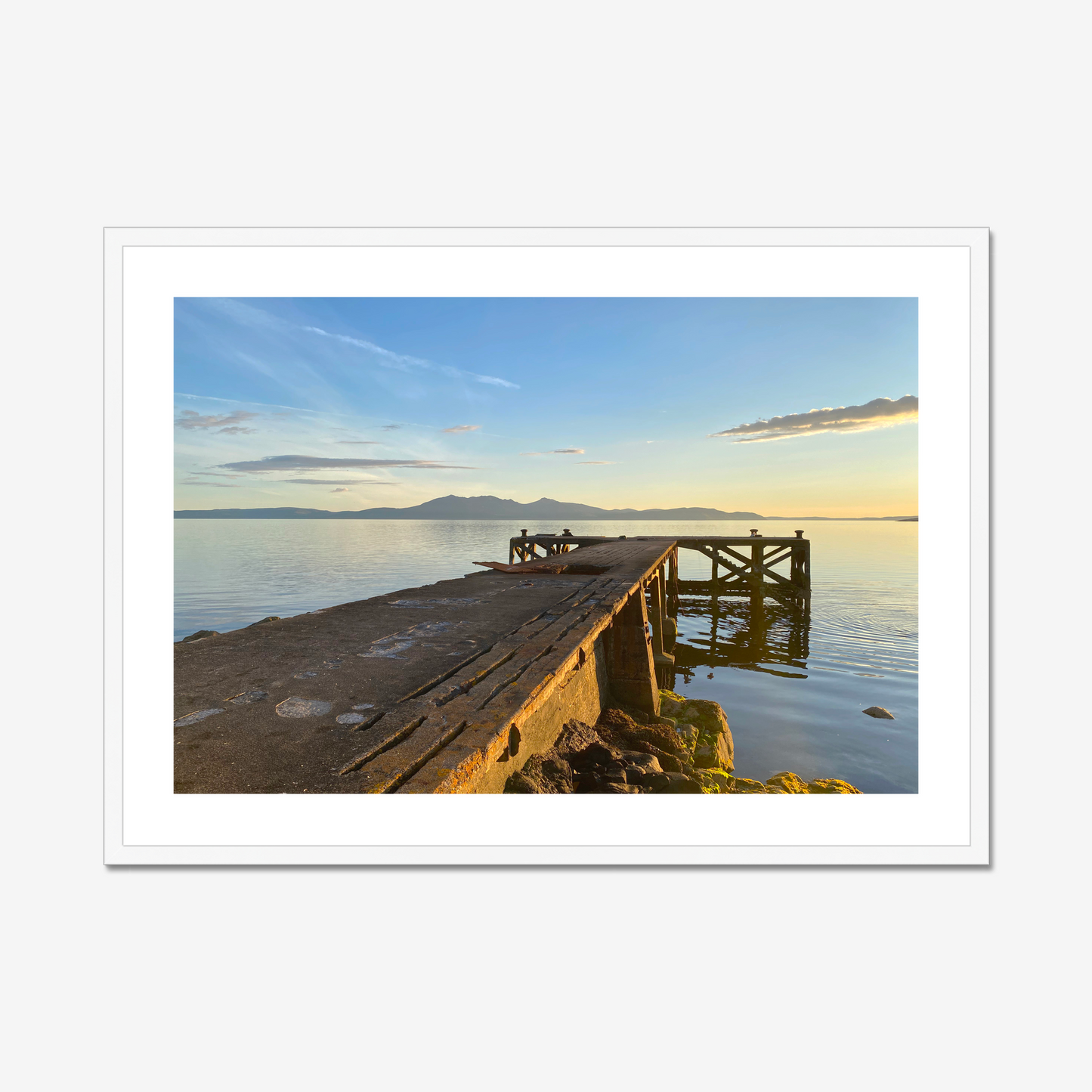 Framed artwork of a sunset over a dock on a gray wall above a white cabinet with decorative items.