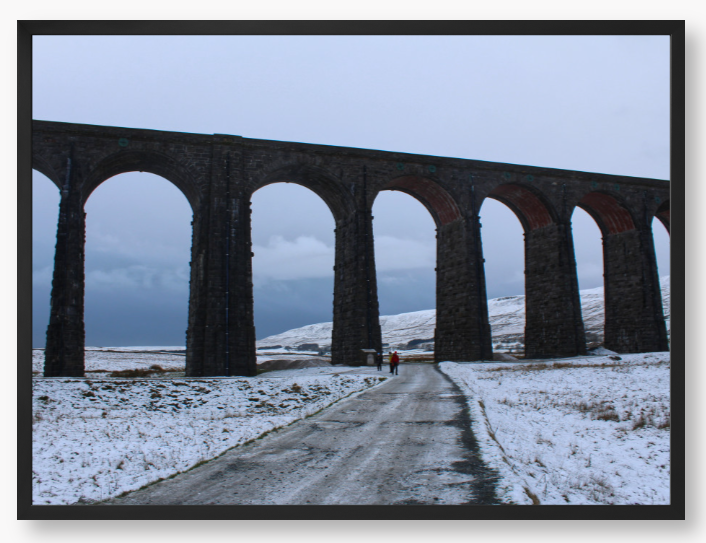 Framed Photo of a Viaduct in a snowy landscape with people walking on a path below.